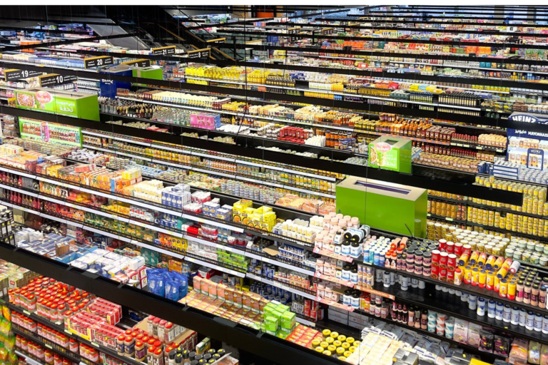 Półki supermarketu wypełnione różnymi kategoriami pakowanej żywności i napojów.